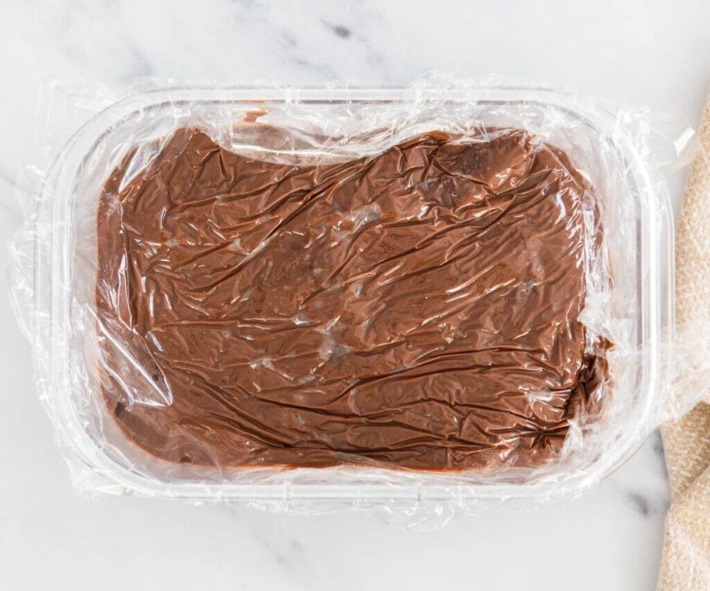 The finished chocolate pastry cream in a glass dish covered with plastic wrap.