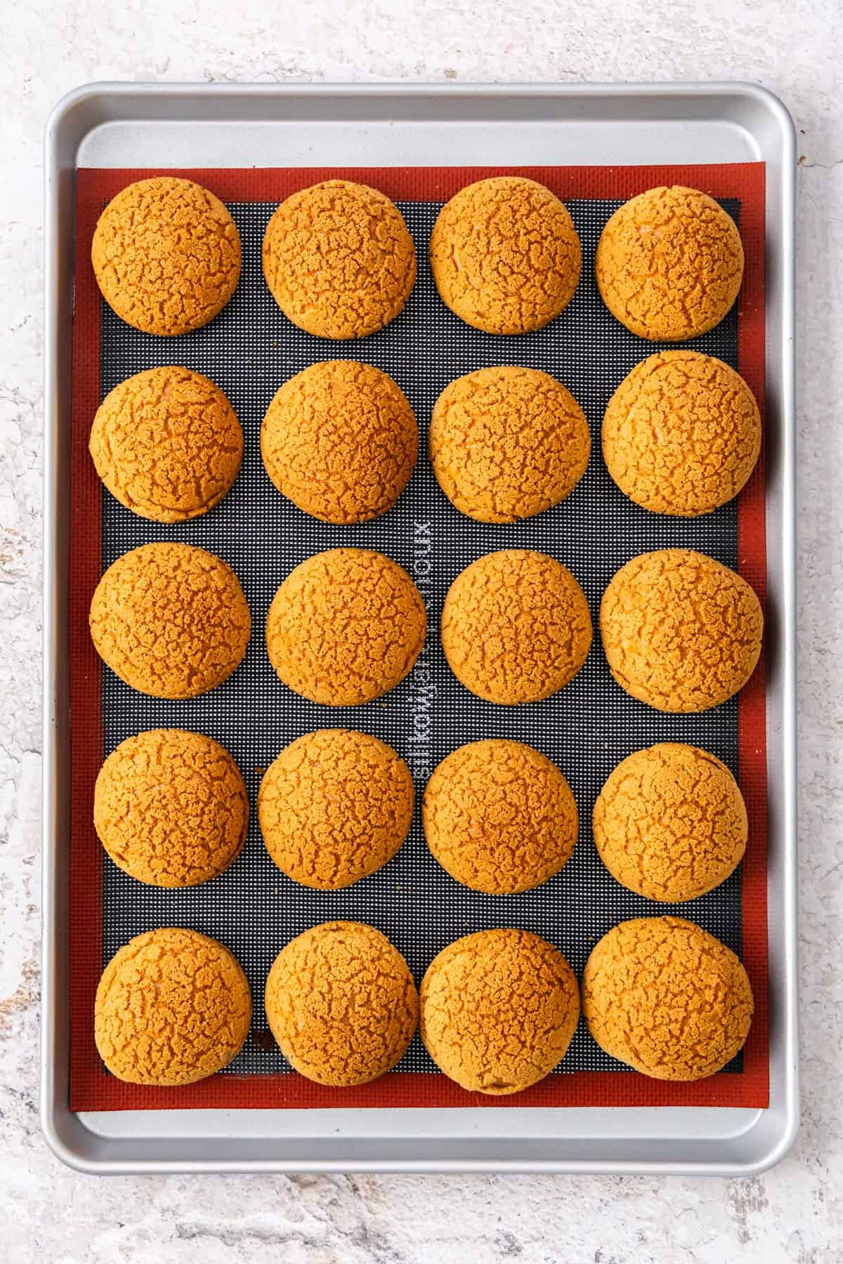 Top down view of 20 choux au craquelin on a baking tray.
