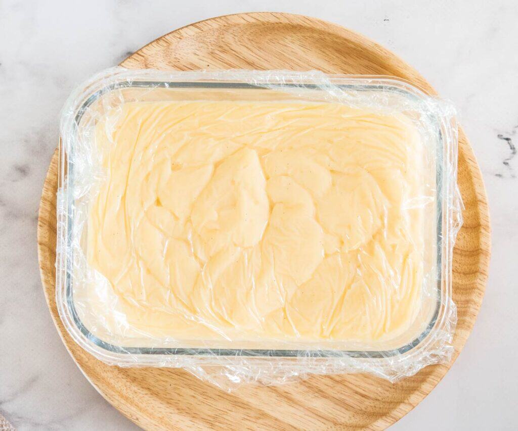 The pastry cream in a bowl with plastic wrap pressed to the surface.