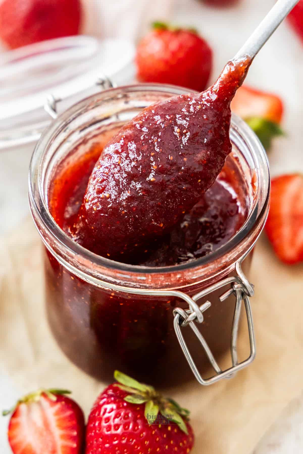 A spoon scooping strawberry jam from a jar.