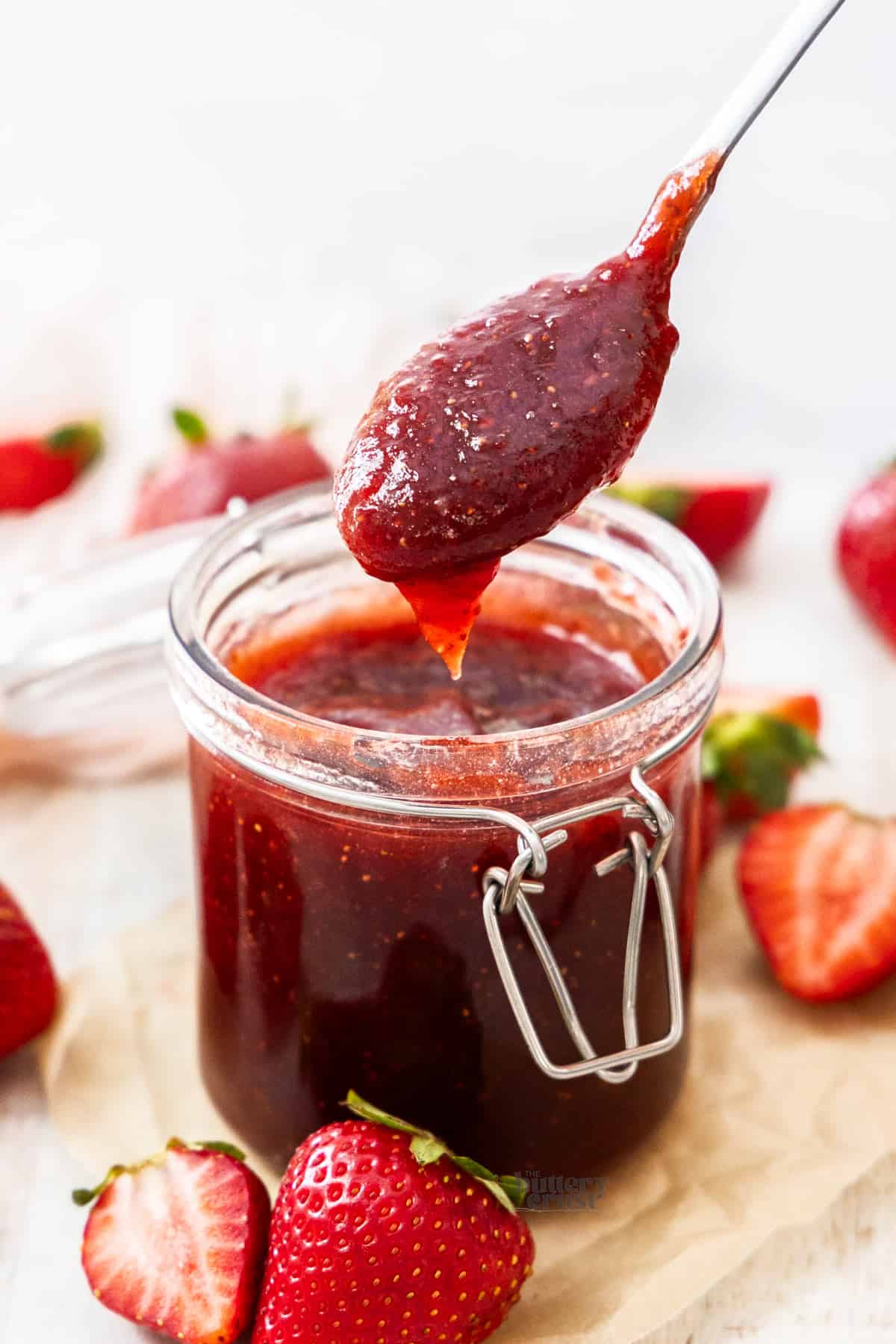 Strawberry jam dropping off a spoon into a jar.
