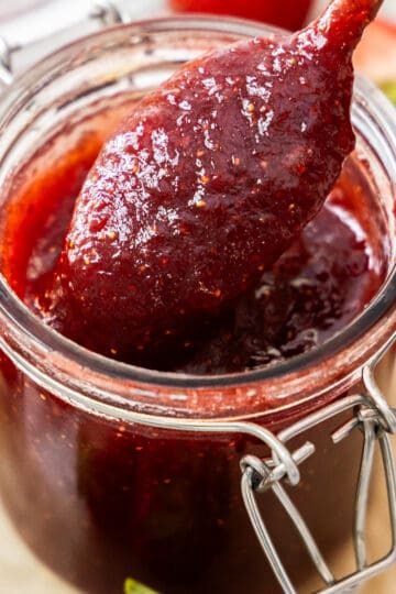 A spoon scooping strawberry jam from a jar.