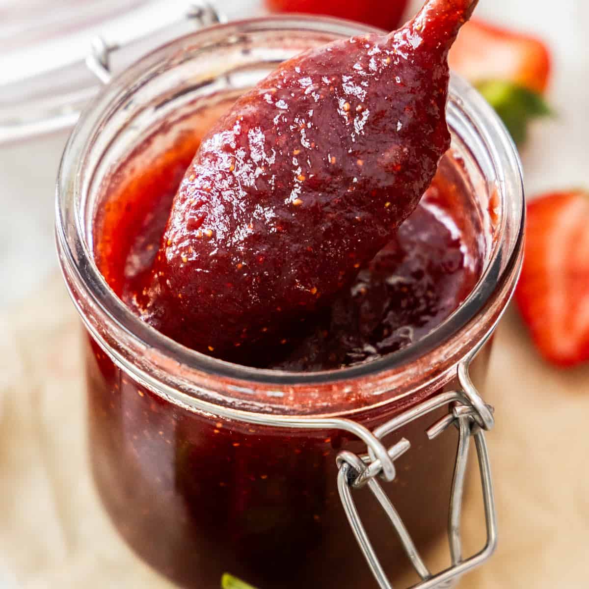 A spoon scooping strawberry jam from a jar.