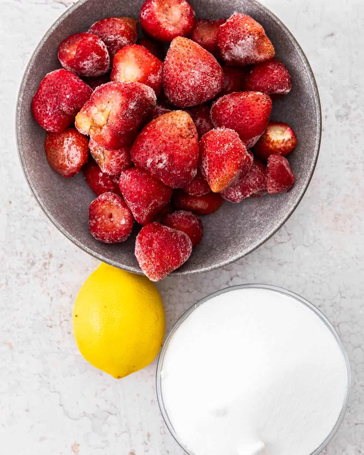 Ingredients for strawberry jam on a stone surface.