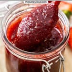 A spoon scooping strawberry jam from a jar with a banner saying "strawberry jam".