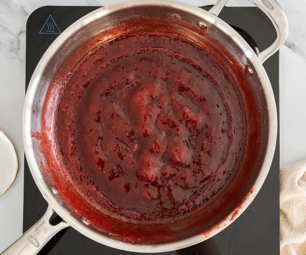 The strawberry jam thickening in a saucepan.