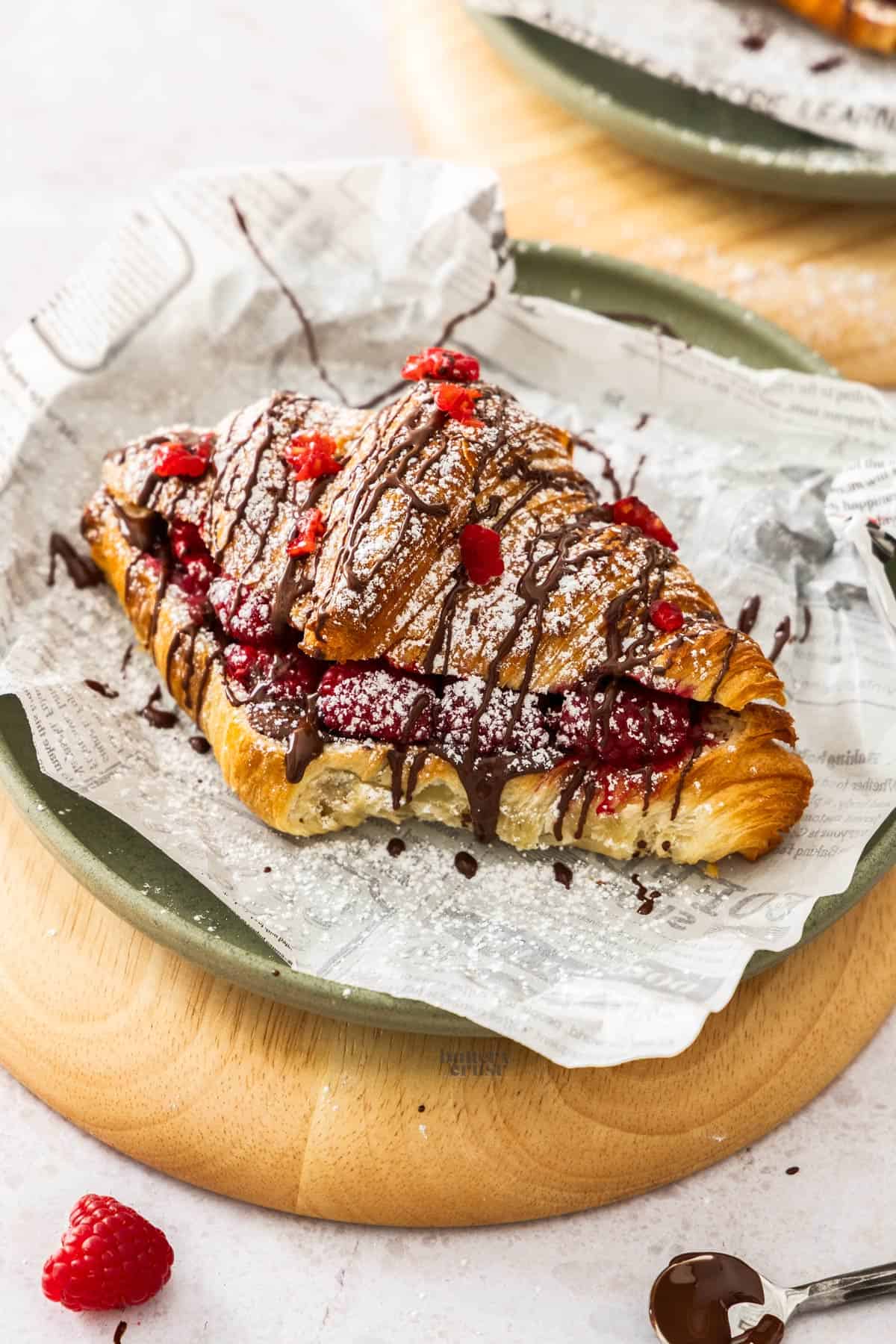 A chocolate raspberry croissant on a green plate, drizzled with chocolate.