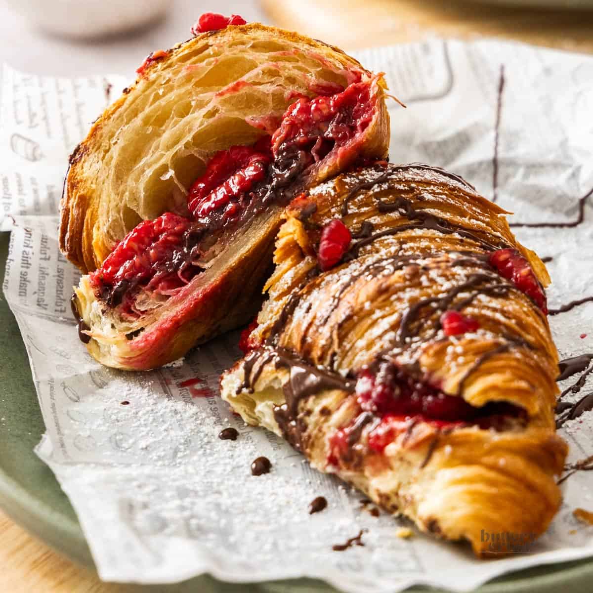 A chocolate raspberry croissant on a plate, cut in half showing the gooey filling.