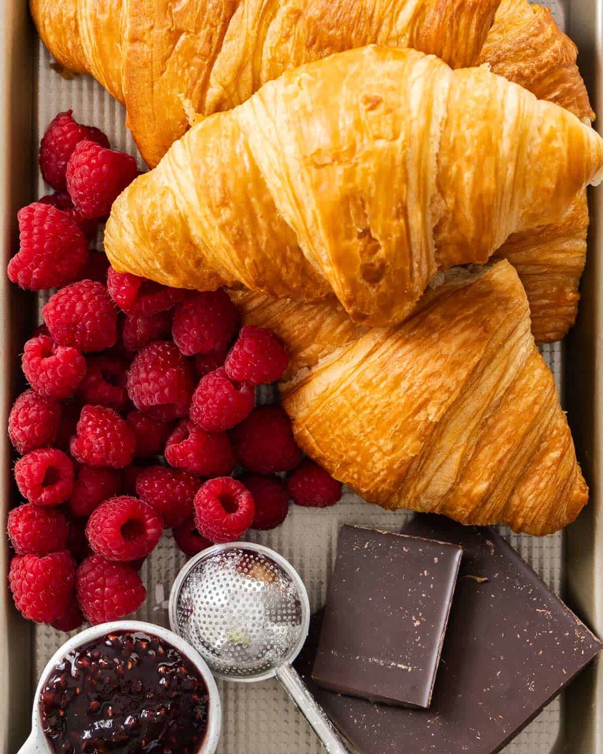 Ingredients for chocolate raspberry croissants on a baking tray.