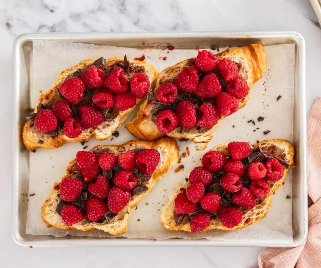 Half croissants topped with chocolate and raspberries.