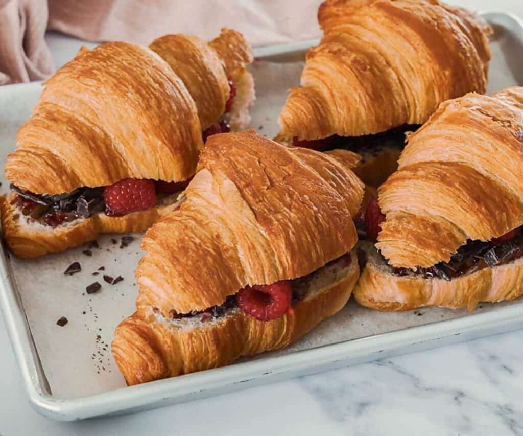 4 croissants filled with chocolate and raspberries on a baking tray.