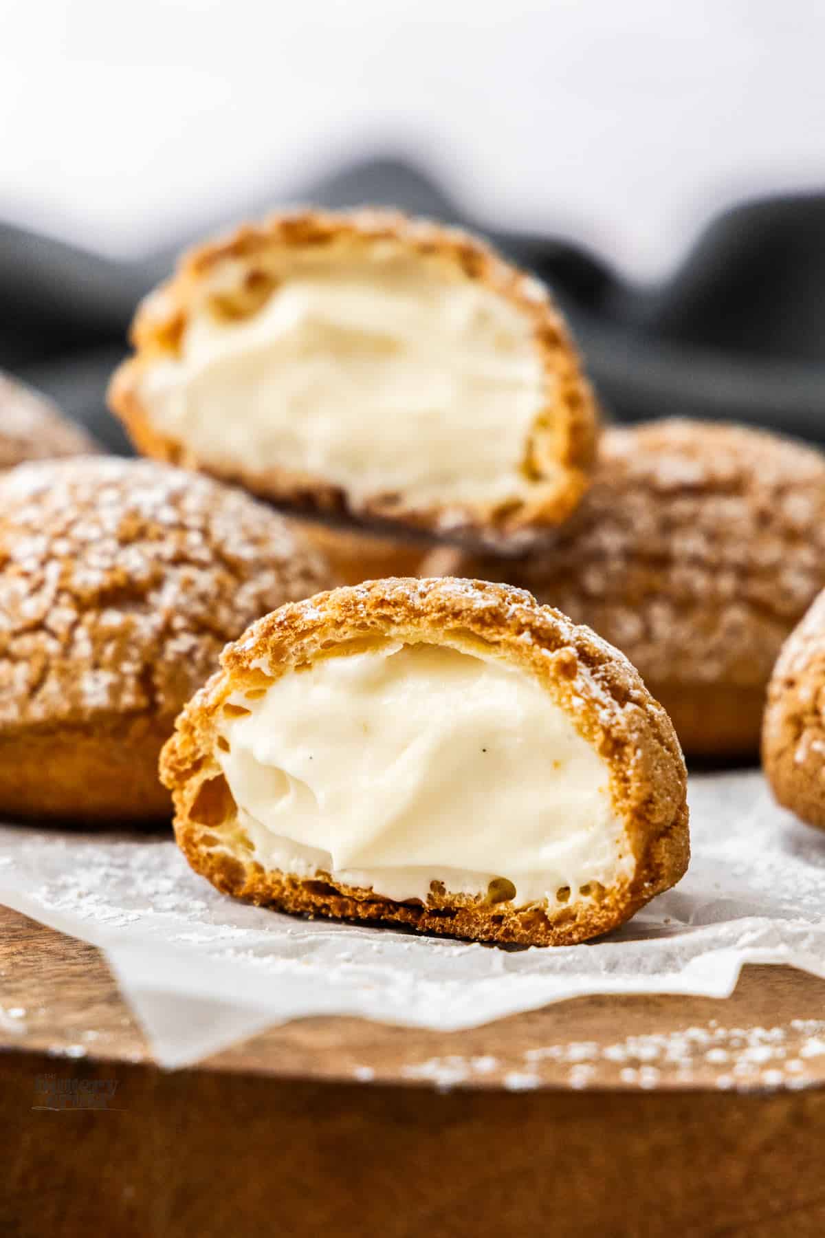 Half a choux a la creme sitting on the edge of a wooden board showing the inside.
