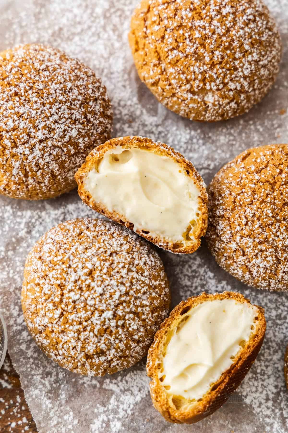 Top down view of a batch of choux a la creme. The centre one is a half, showing the filling inside.