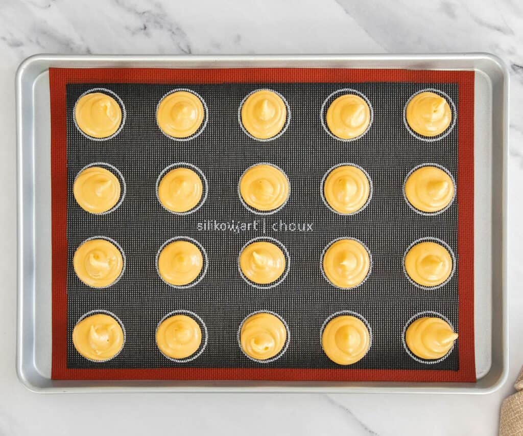 Choux domes piped onto a baking sheet.