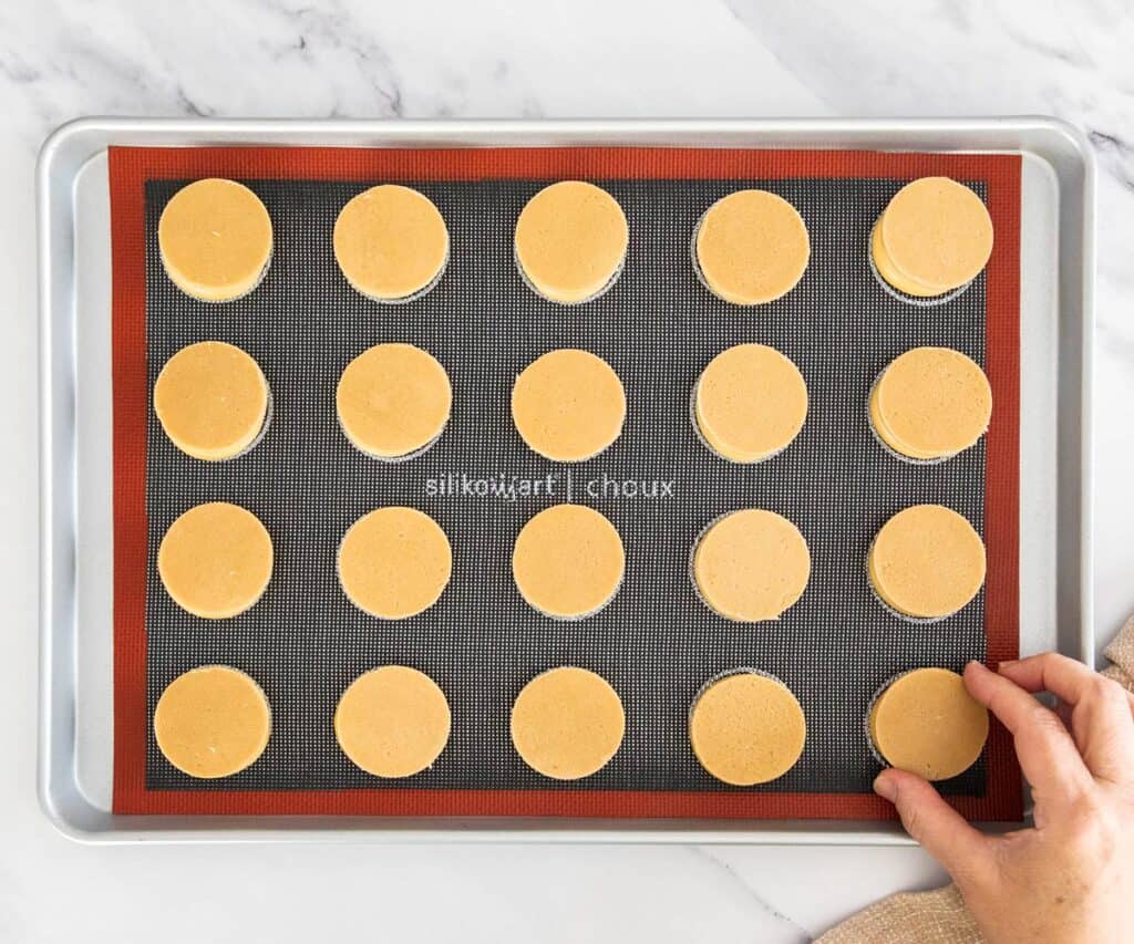 A hand placing the craquelin rounds on top of the choux pastry.