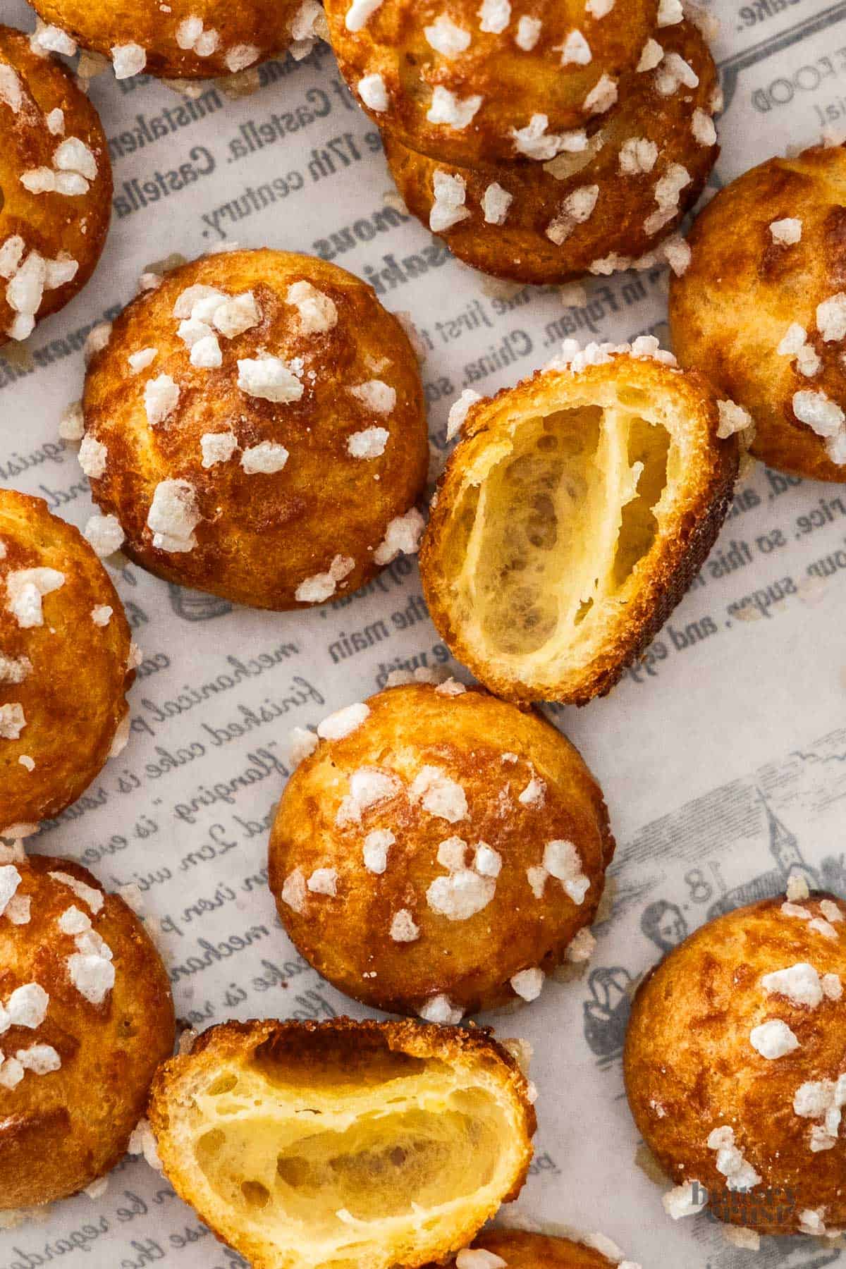 Top down view of a batch of chouquettes. One has been cut in half to show the inside.