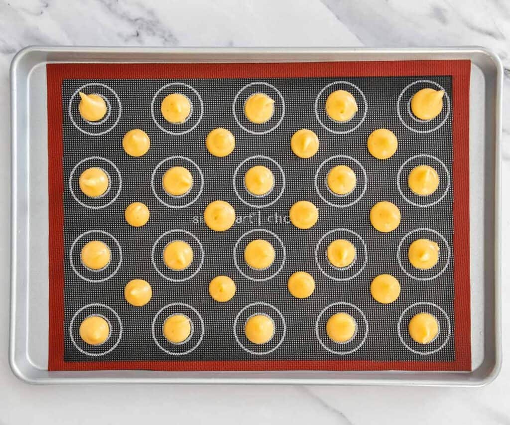 Top down view of mini mounds of choux dough on a baking tray.
