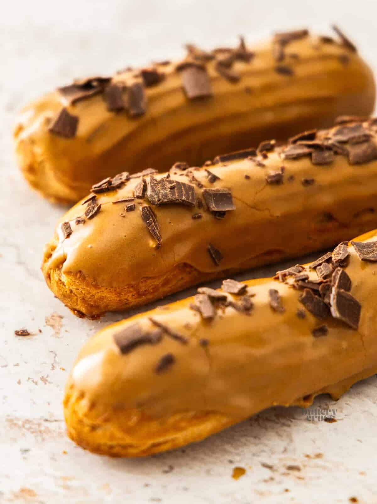 3 coffee eclairs lined up on a concrete surface.