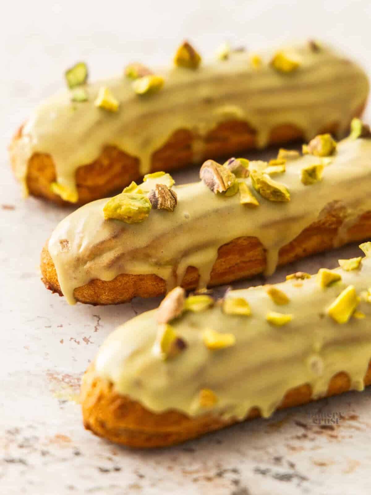 3 pistachio eclairs lined up on concrete surface.