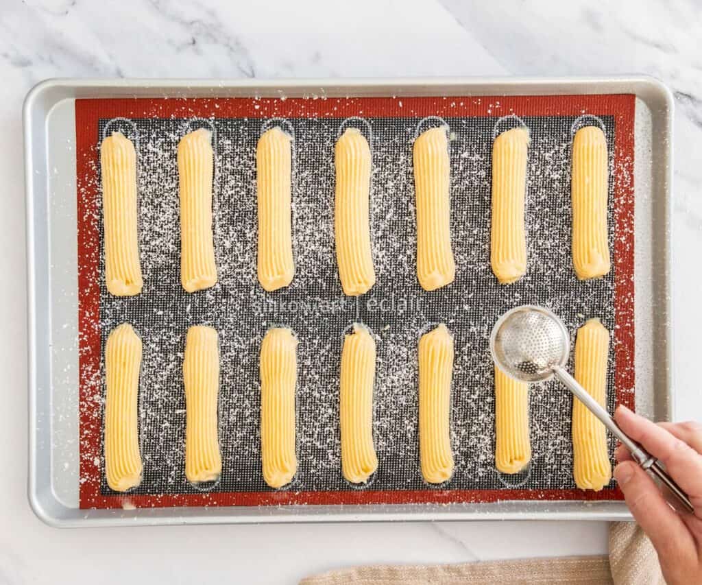 Icing sugar being piped over the eclairs.