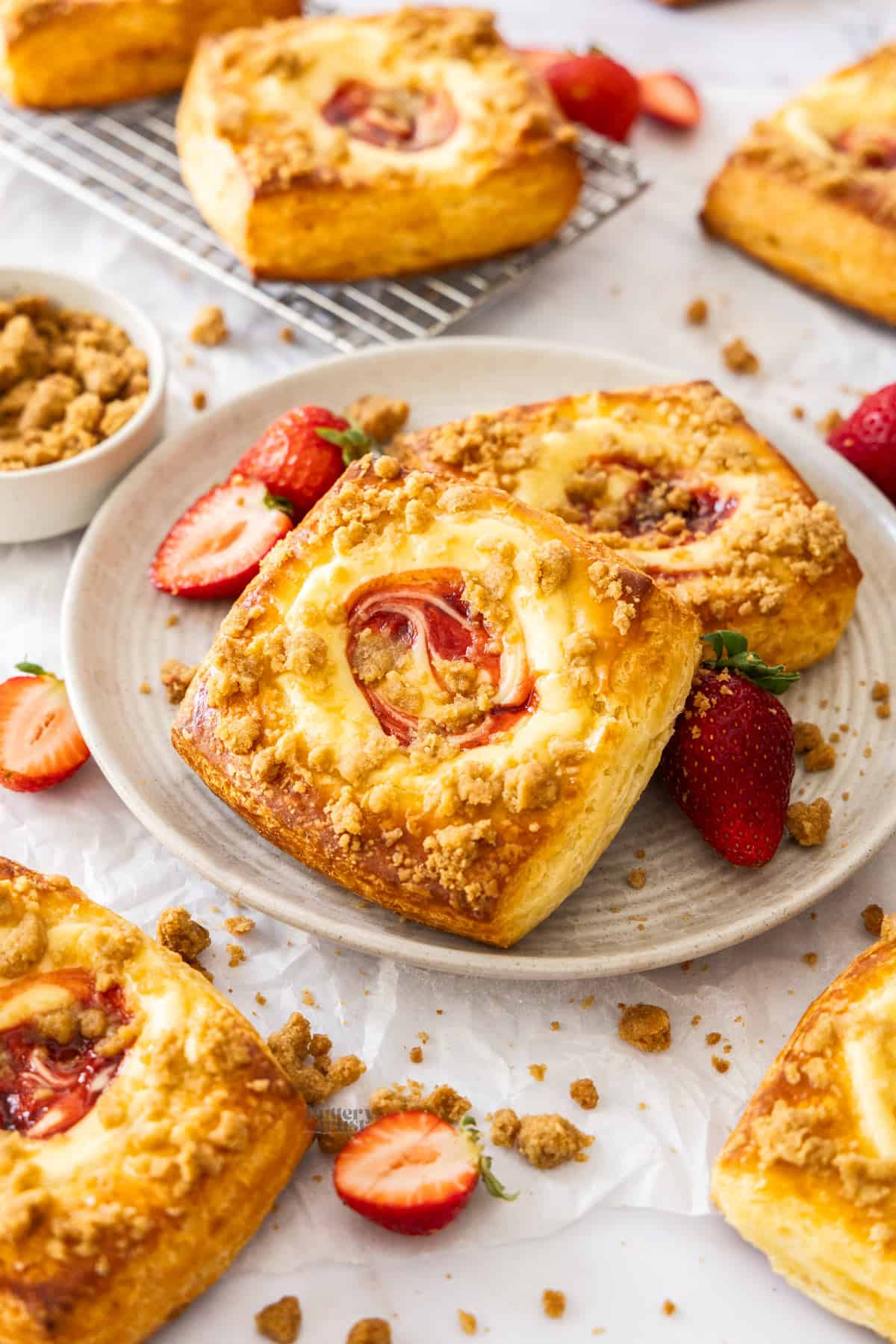 2 strawberry cream cheese Danishes on a plate with more scattered around.