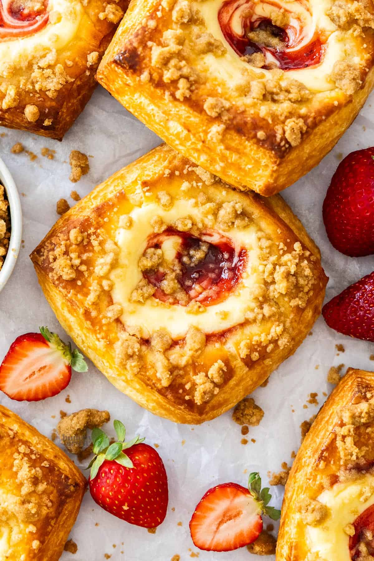 Top down view of strawberry cheesecake Danishes surrounded by strawberries and crumbs.