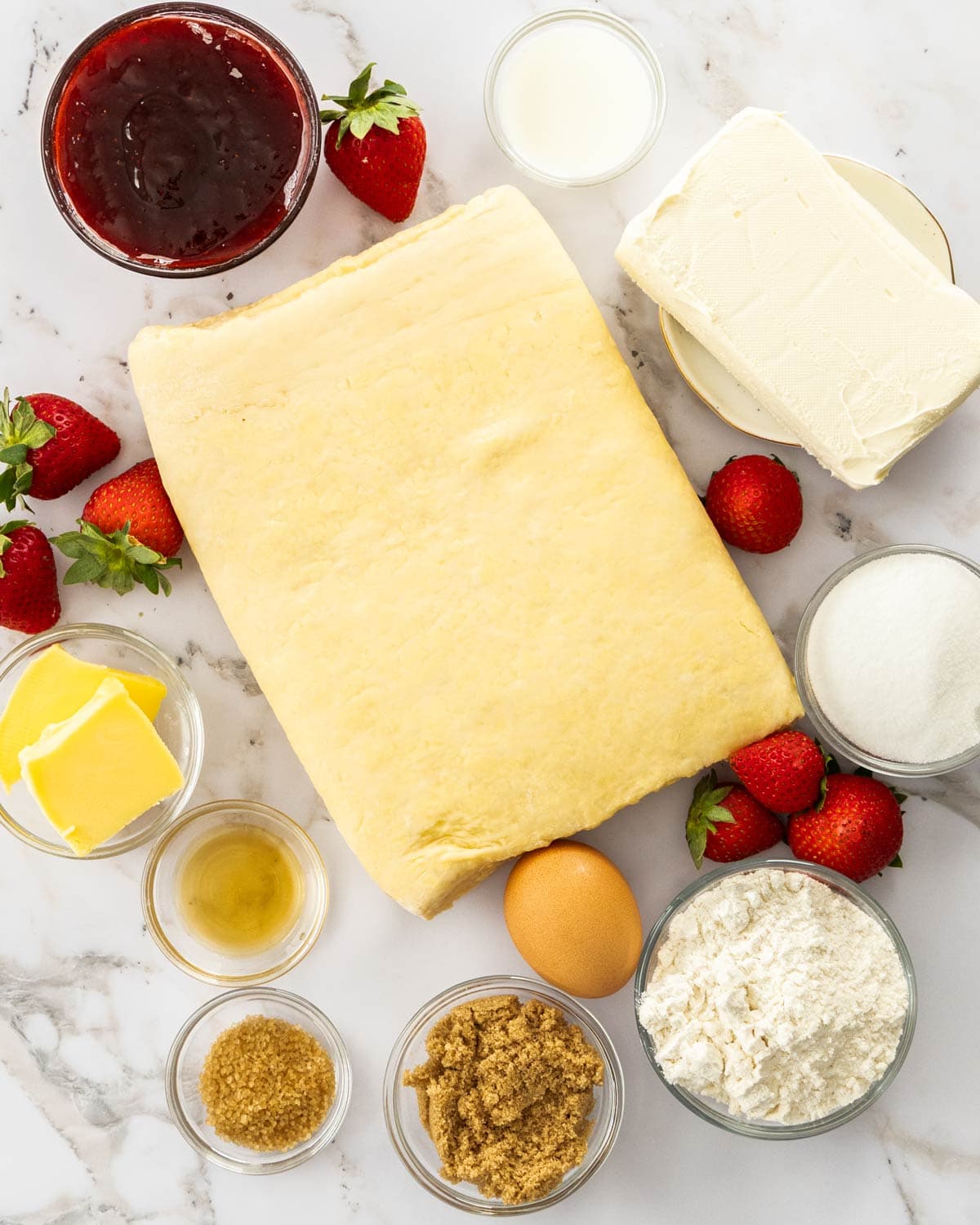 Ingredients for strawberry cheesecake Danish on a marble surface.