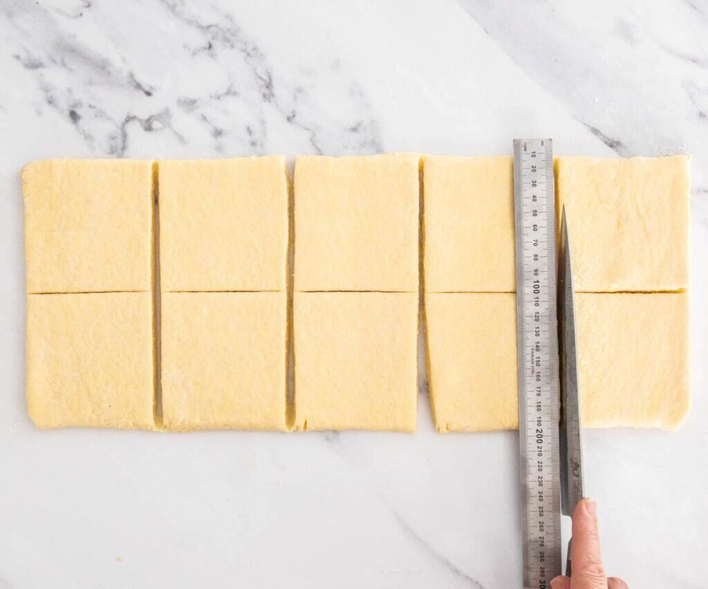 Danish pastry dough being cut into 10 squares.