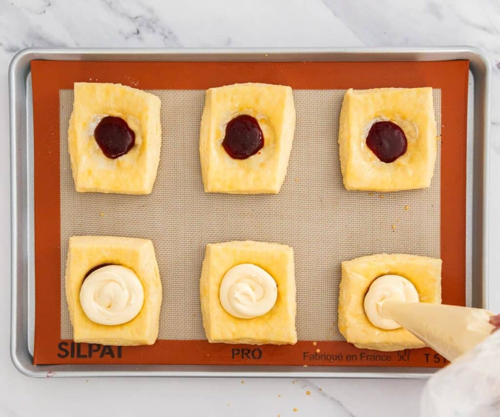 Cheesecake filling being piped over the top of jam in a Danish.