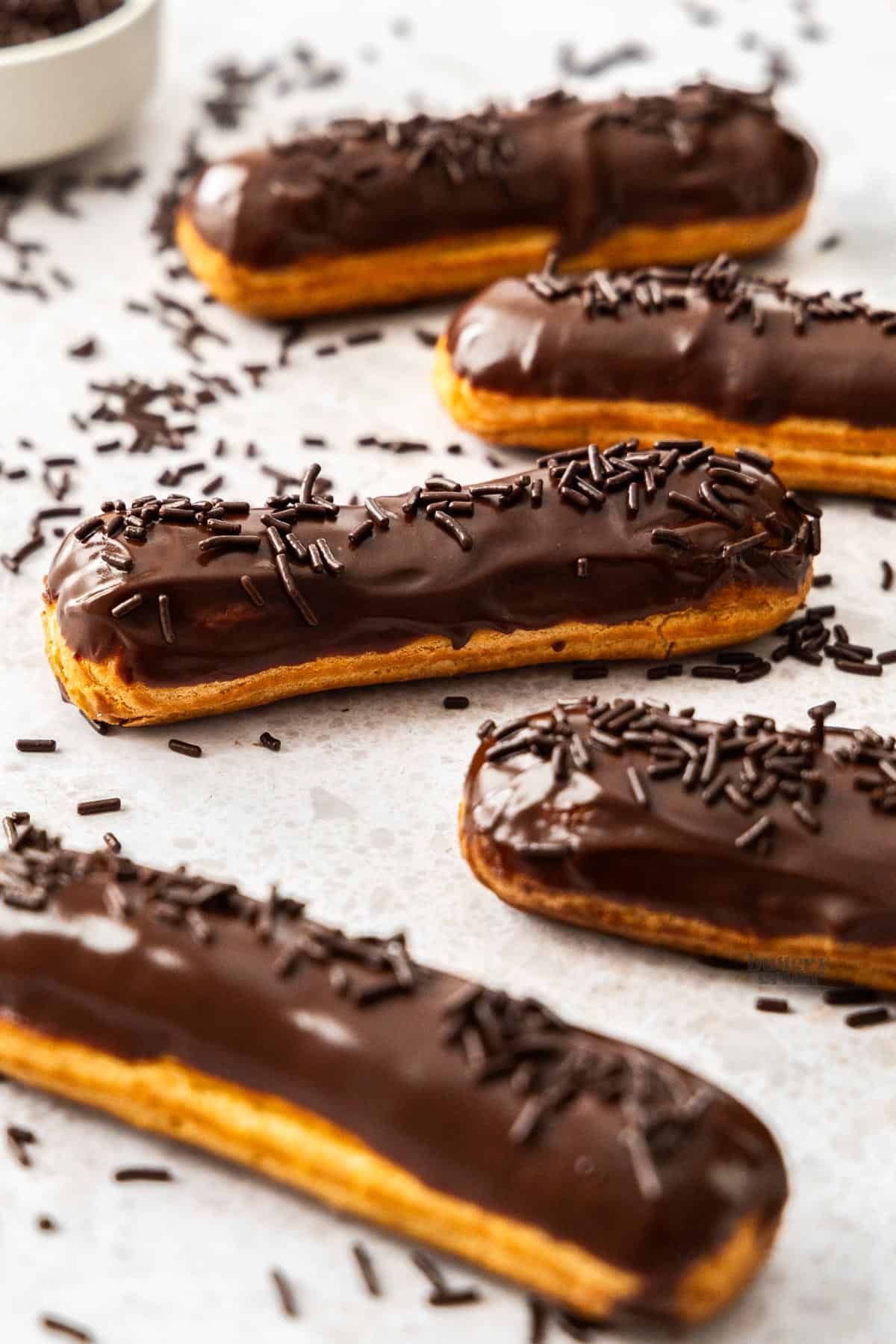 5 chocolate coated eclairs surrounded by chocolate sprinkles.