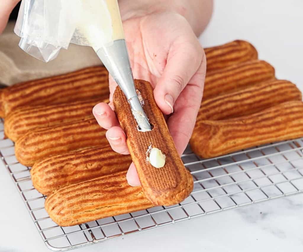 Pastry cream being piped into the base of an eclair.