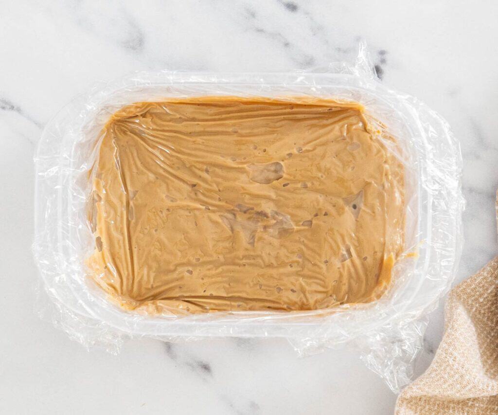 Coffee pastry cream in a container with plastic wrap pressed to the surface.