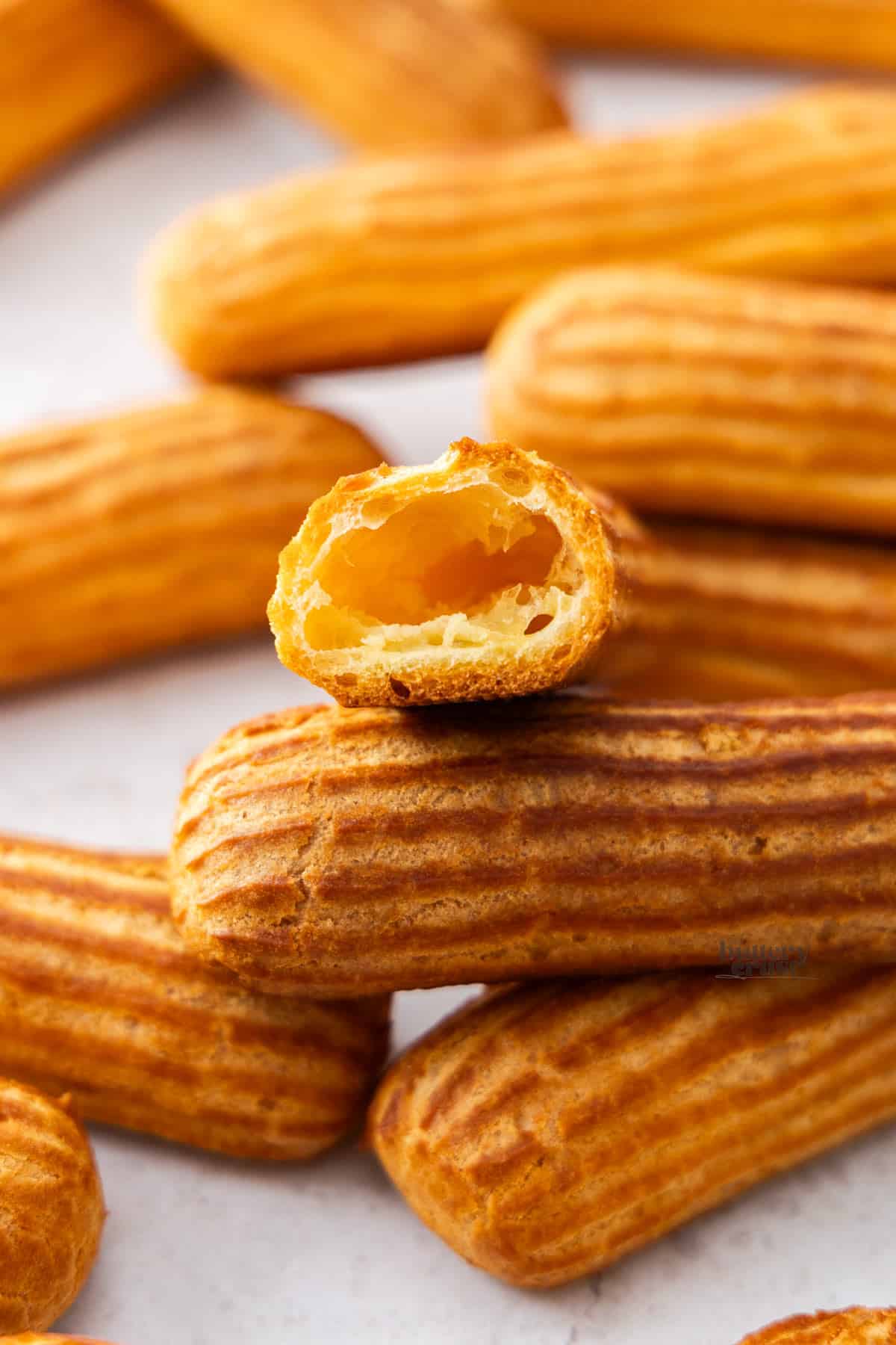 A pile of eclair shells with one cut open and turned toward the camera to show the hollow inside.