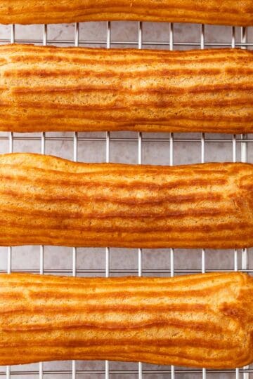 Top down view of the tops of 3 eclairs sitting on a wire rack.