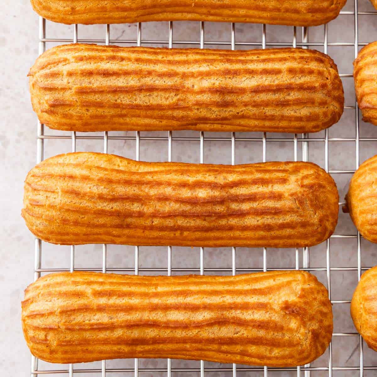 Top down view of the tops of 3 eclairs sitting on a wire rack.