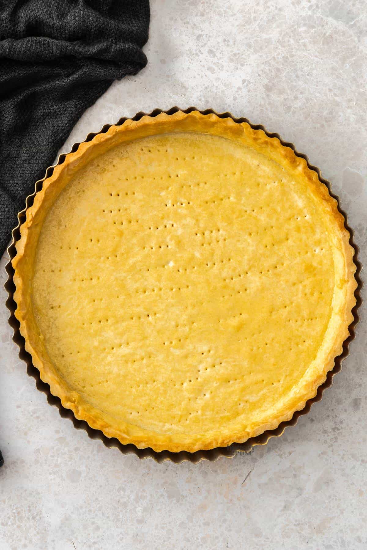 Top down view of a Pâte Sucrée tart shell on a stone surface.