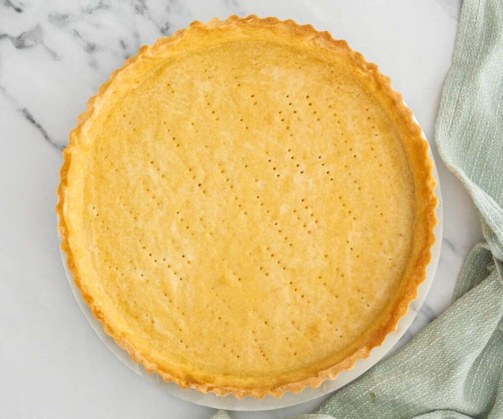 The baked Pâte Sucrée tart shell on a marble platter.