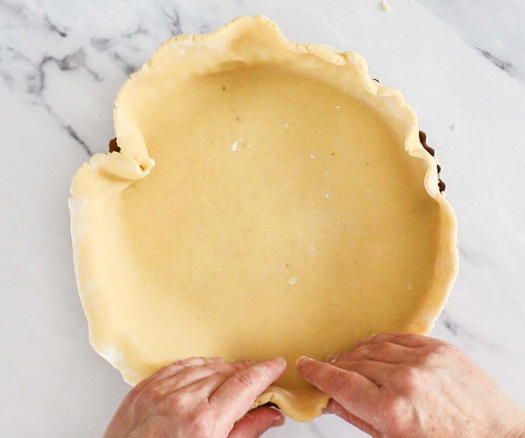 Two hands gently arranging the pastry into a tart pan.