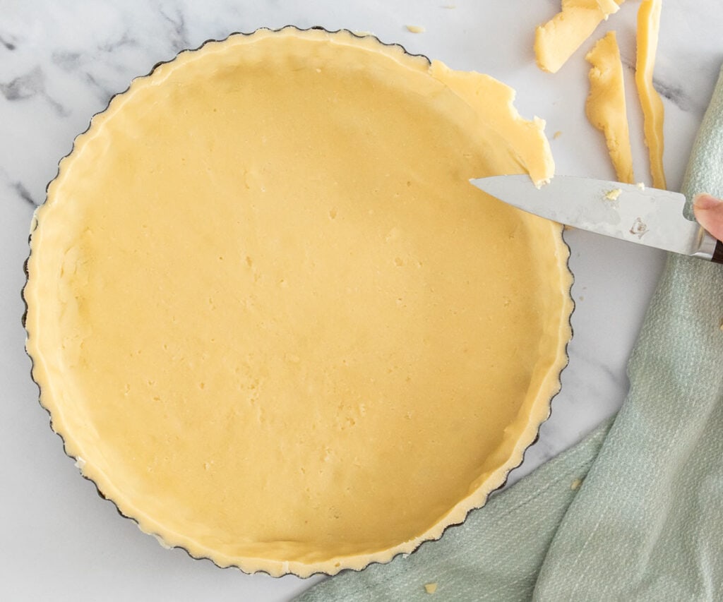 A small knife trimming away excess dough from the edge of the tart shell.