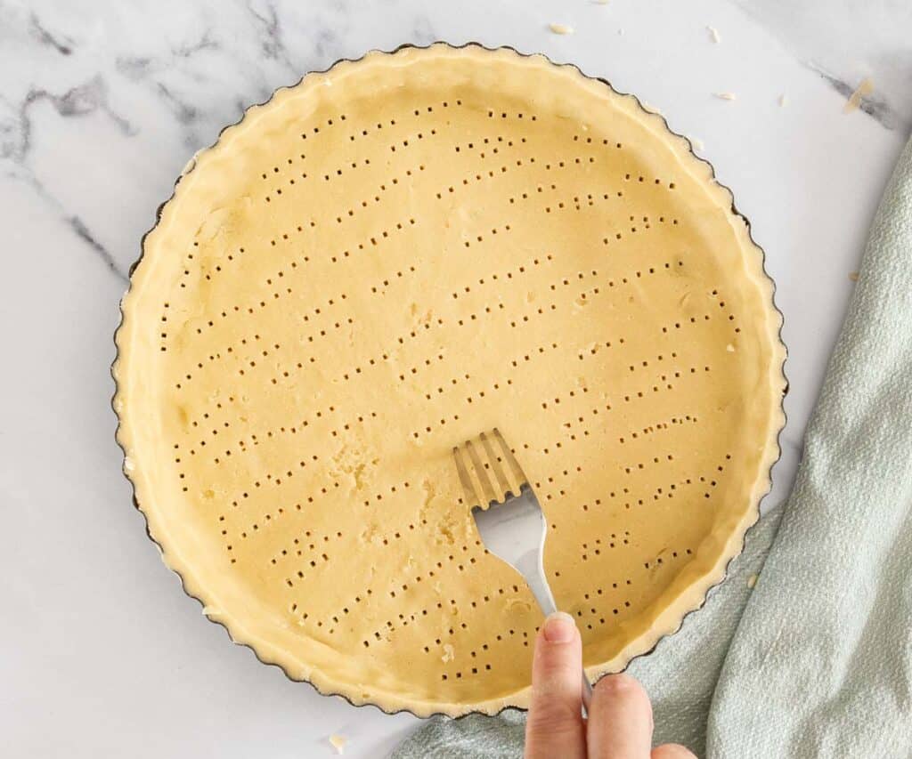 A fork poking holes into the base of the tart shell.