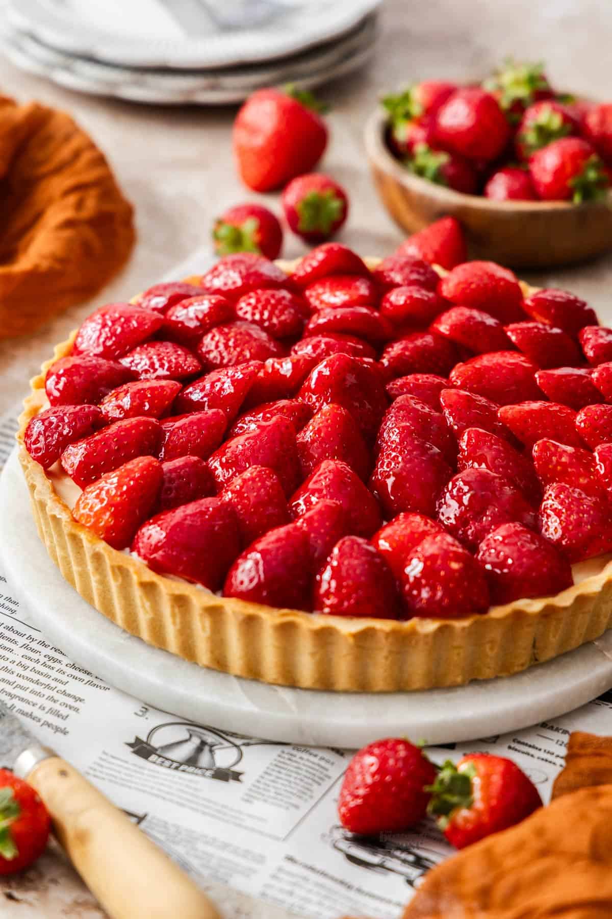 A whole strawberry tart on a marble platter shown at a 45 degree angle.