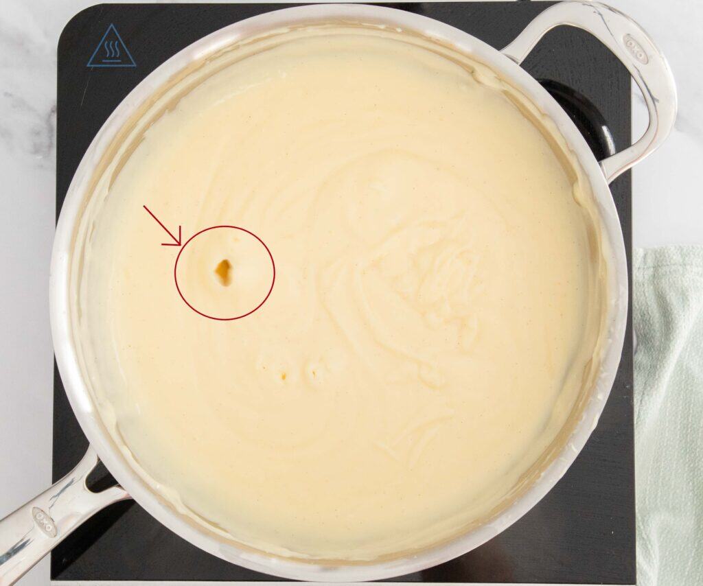 A saucepan with the pastry cream bubbling, with an arrow pointing to the bubbles that are coming up.