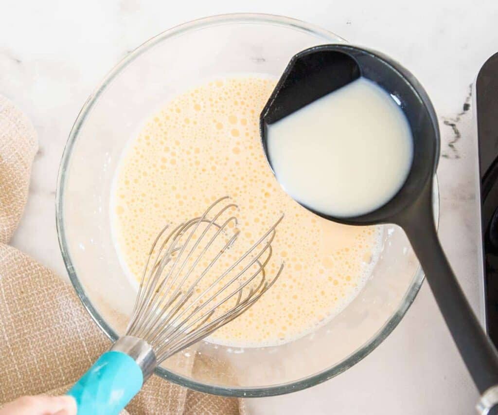Adding hot milk to the egg yolk mixture.
