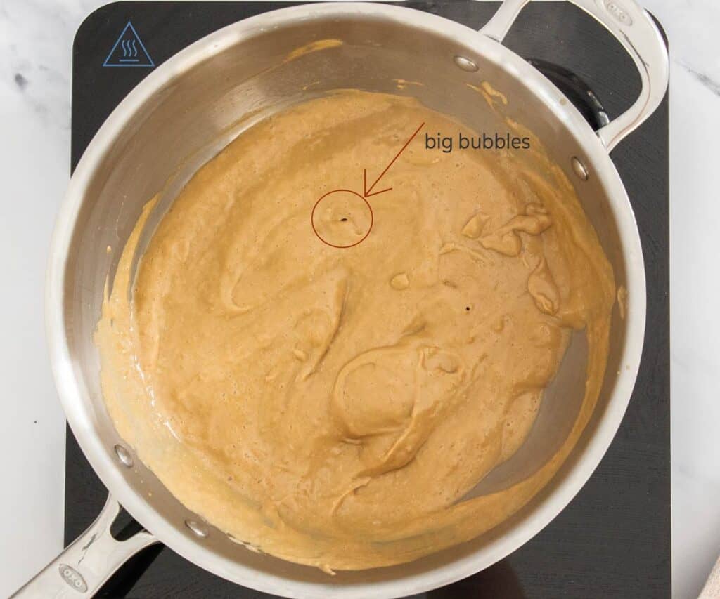 The thickened coffee pastry cream showing bubbles where it is boiling in the pan.