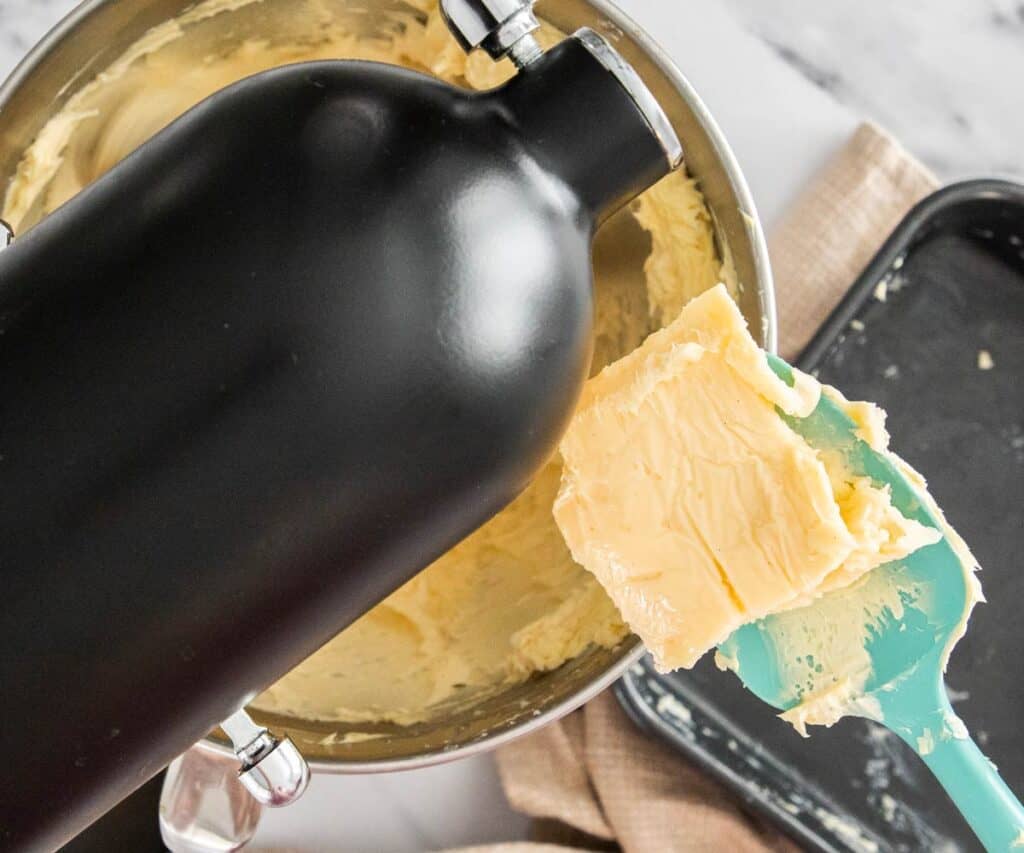 A spoon dropping set pastry cream into a stand mixer bowl.