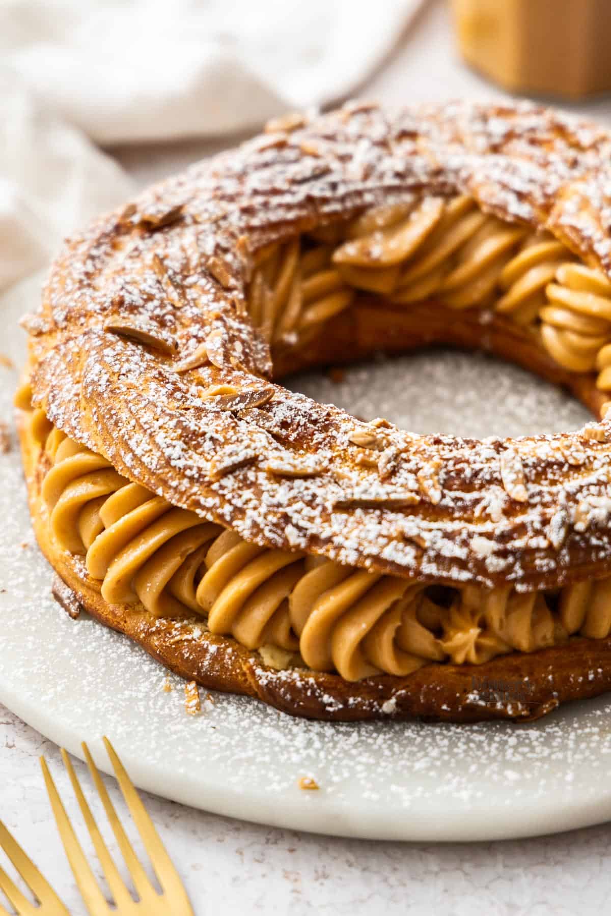 A whole Paris-Brest on a marble platter, dusted with icing sugar.