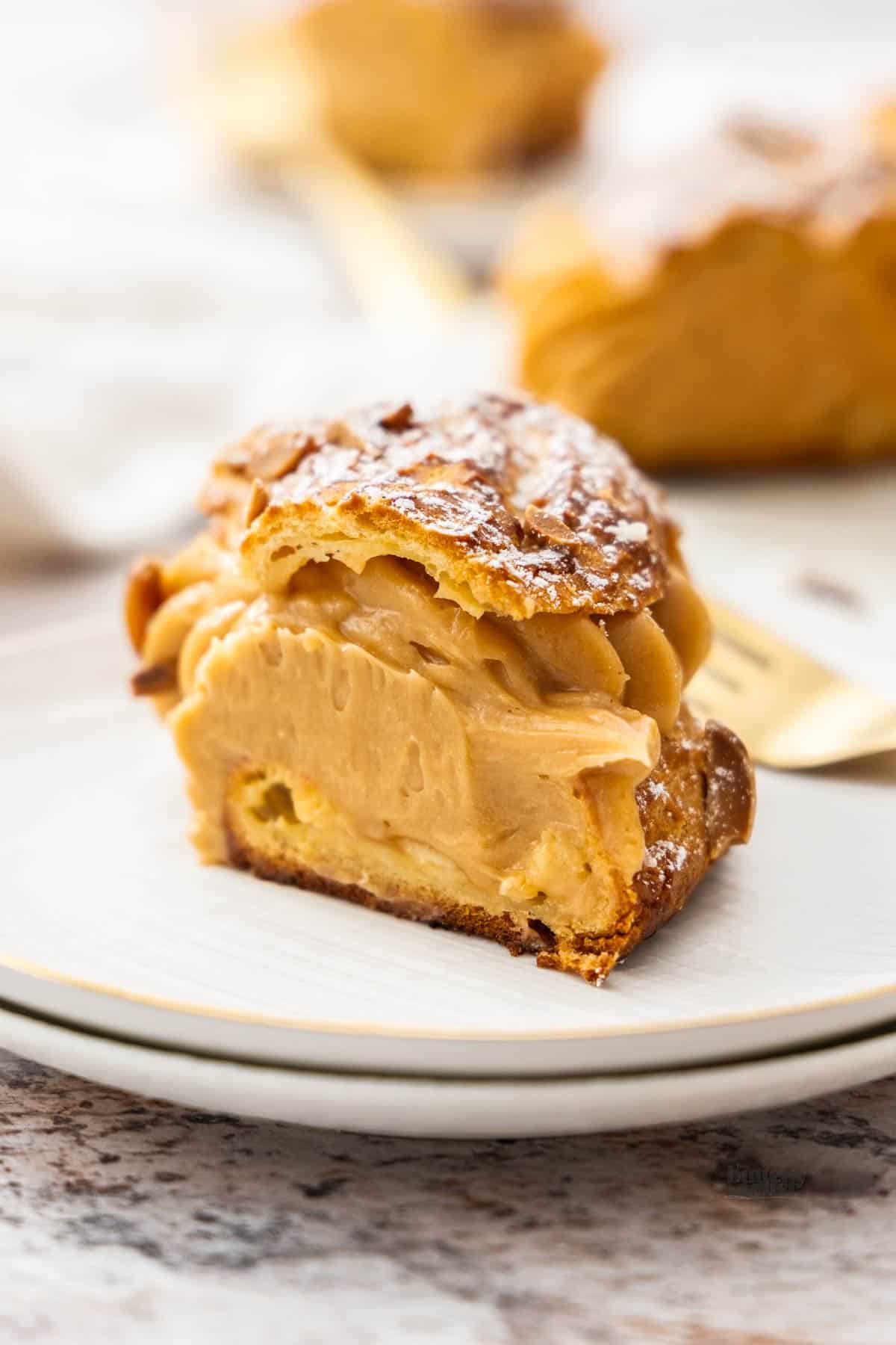 A slice of Paris-Brest on a dessert plate showing the decadent mousseline cream inside.