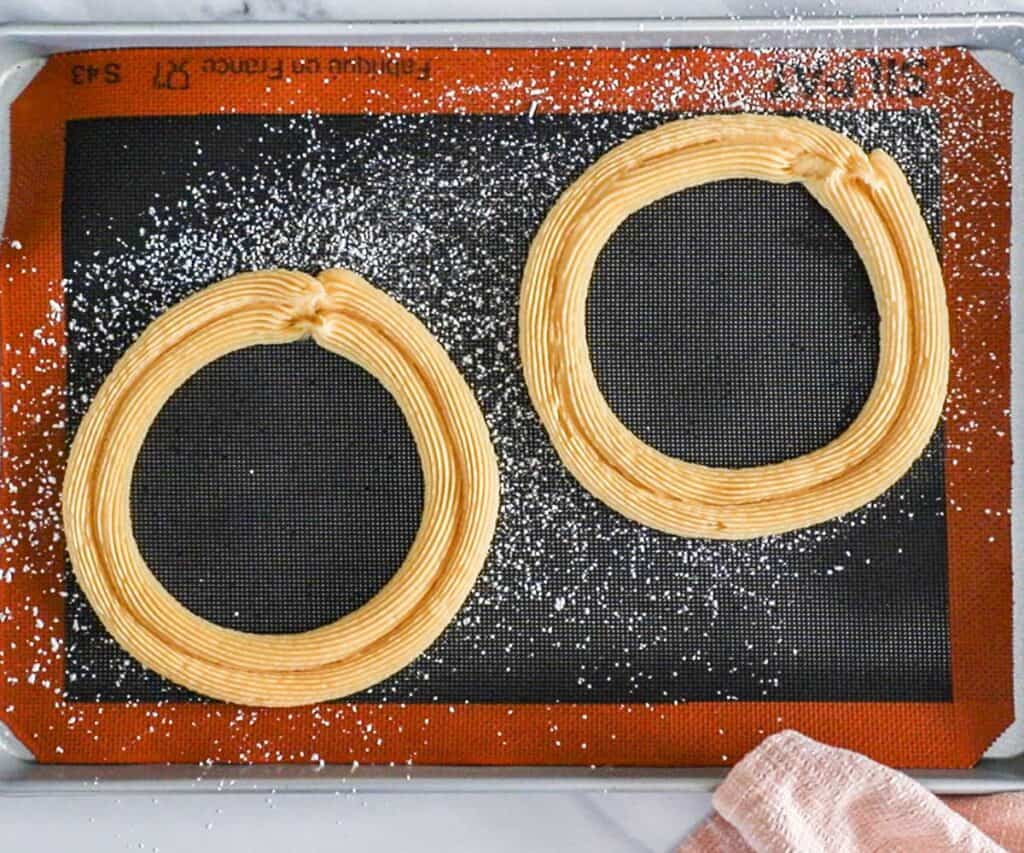 Two circles made up of two rings each of dough piped onto the baking sheet.