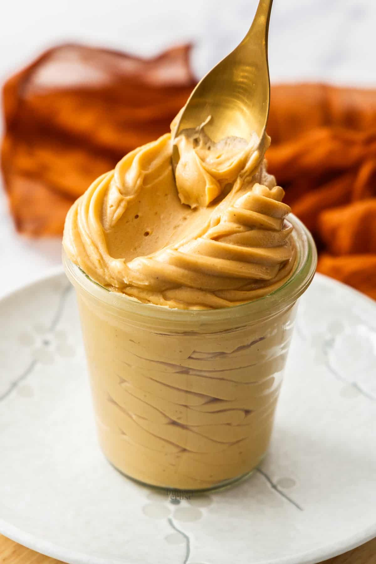 A spoon being dragged through praline cream to show its silky-smooth texture.