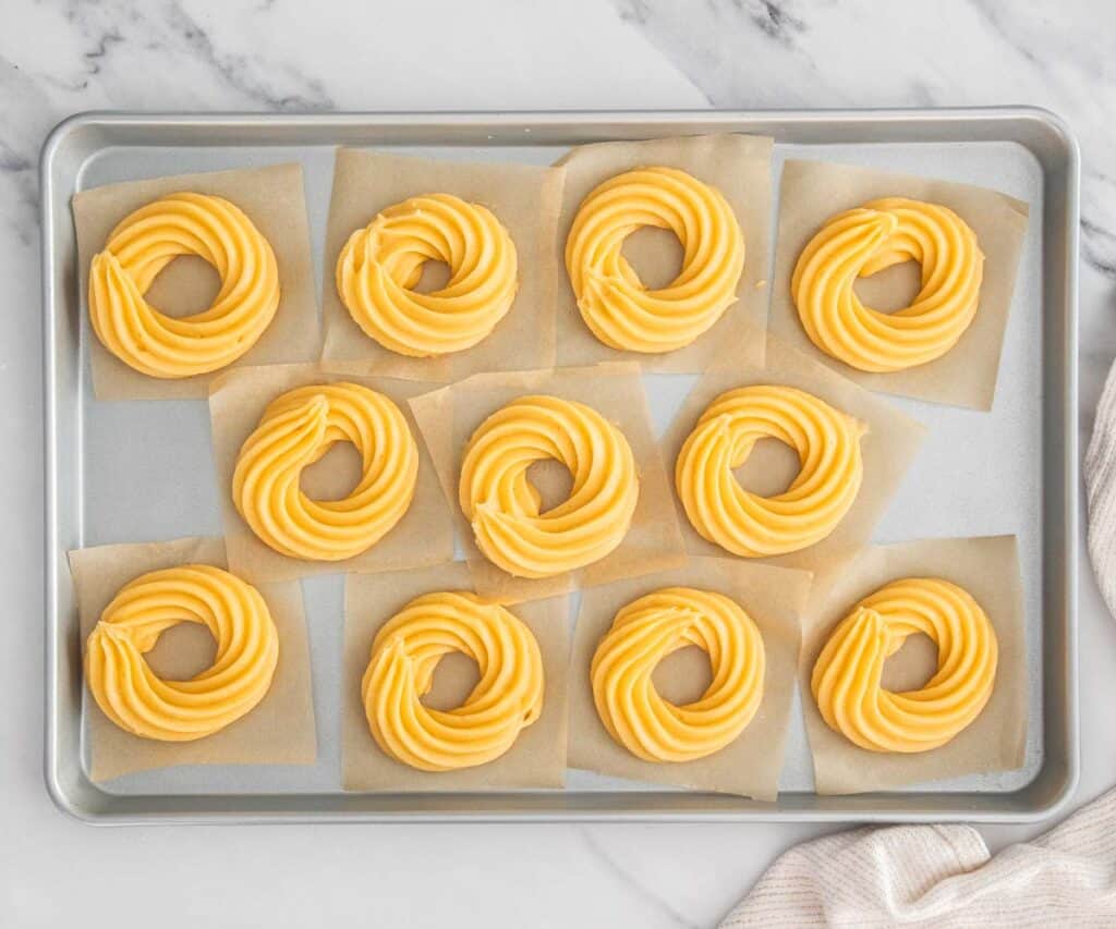 Top down view of eleven circles of choux pastry piped onto squares of parchment paper.